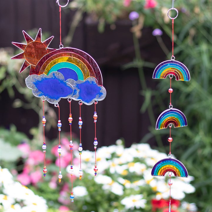 Decorative sun catcher with rainbows, sun, and clouds hanging in a garden.