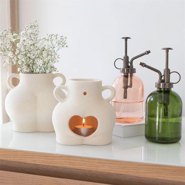 Decorative items including a ceramic candle holder, glass bottles, and a vase with flowers on a white surface.