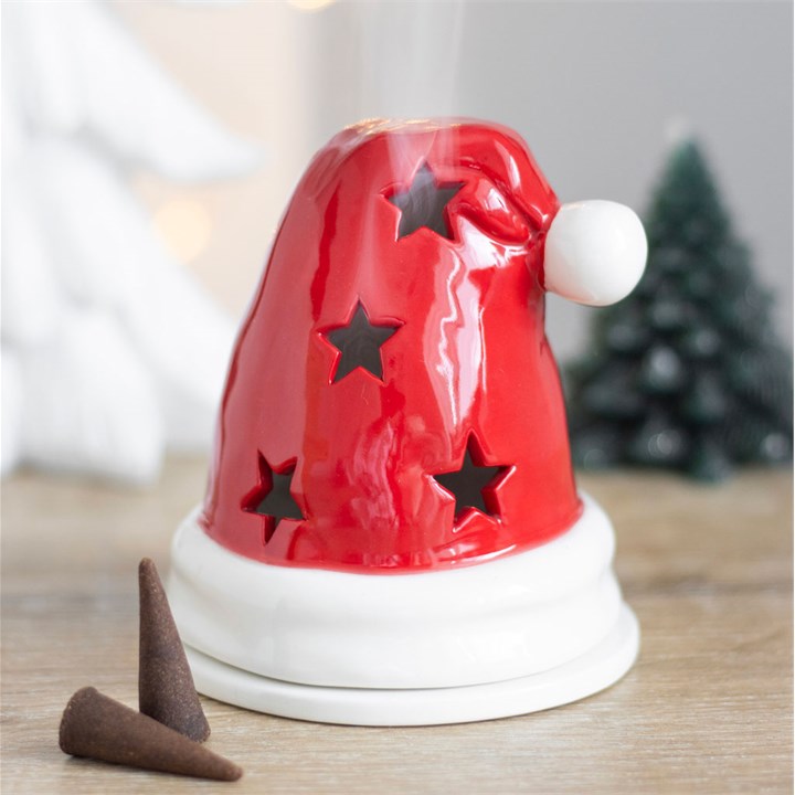 Red Santa hat-shaped diffuser with stars on a wooden surface, Christmas tree in the background