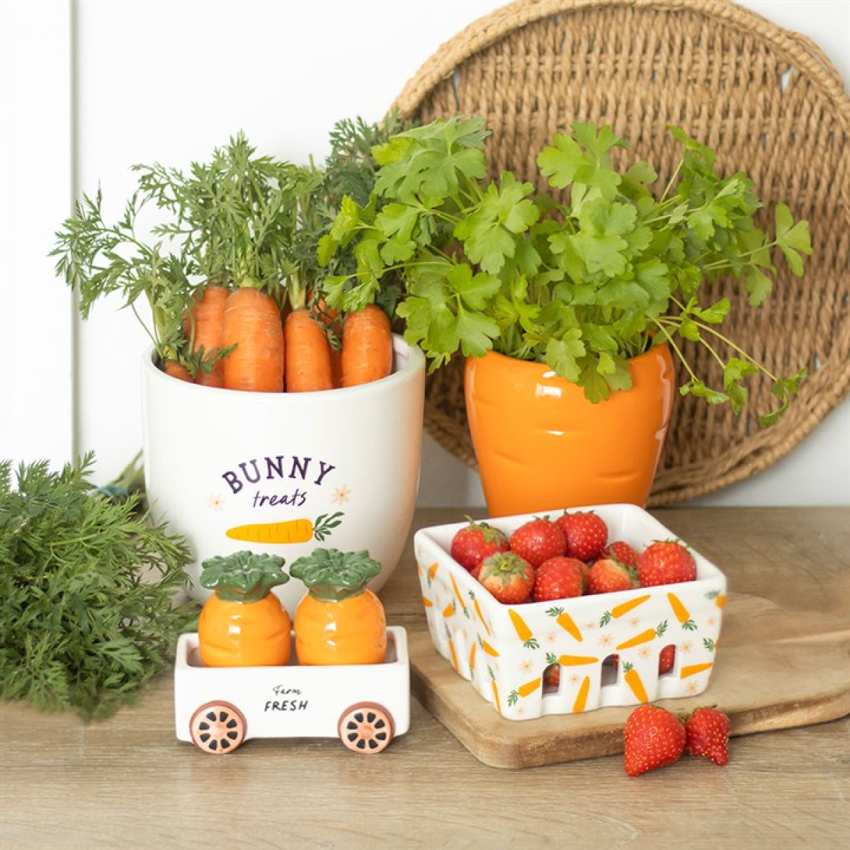 Decorative items including a white container with carrots, an orange planter with greenery, and a small cart with strawberries on a wooden surface.
