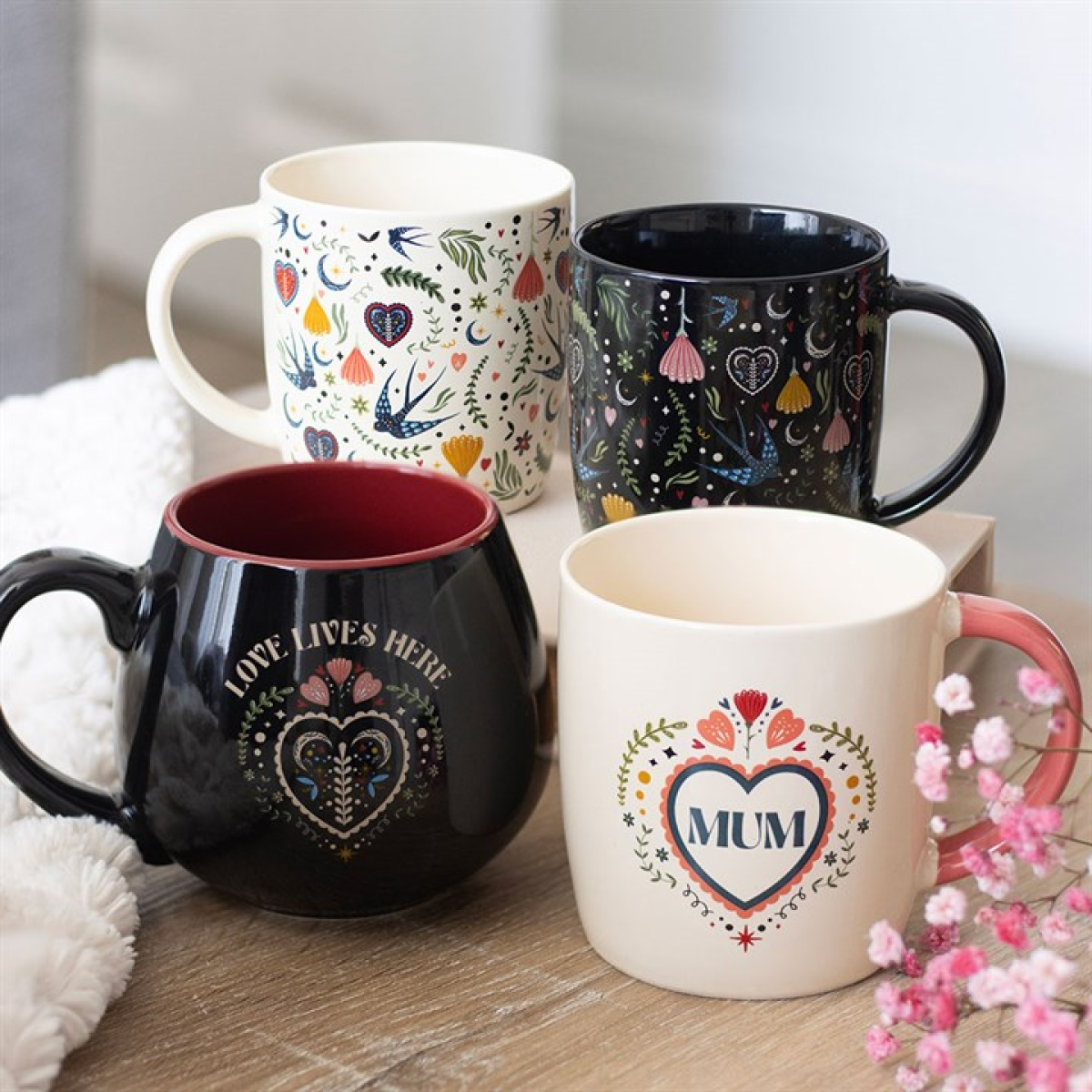 Four mugs with decorative designs on a wooden surface.
