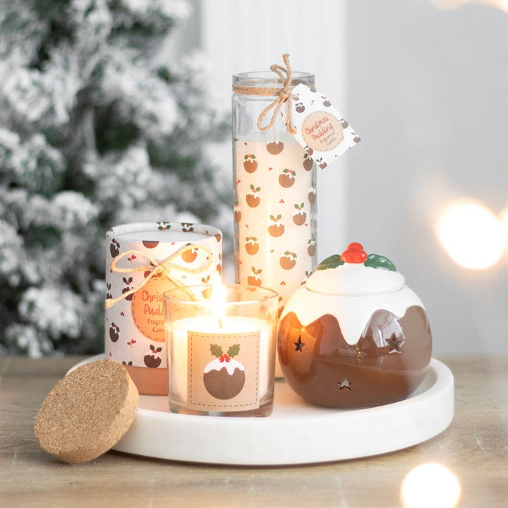Decorative candles and a pudding-shaped ornament on a white plate with a Christmas tree in the background.
