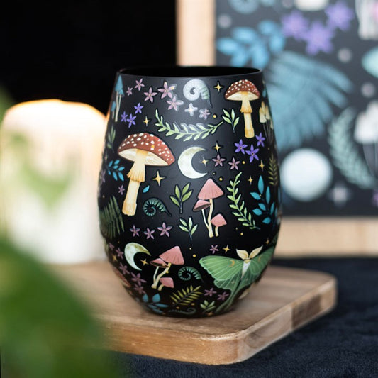 Decorative wine glass with mushroom and nature pattern on a wooden coaster.