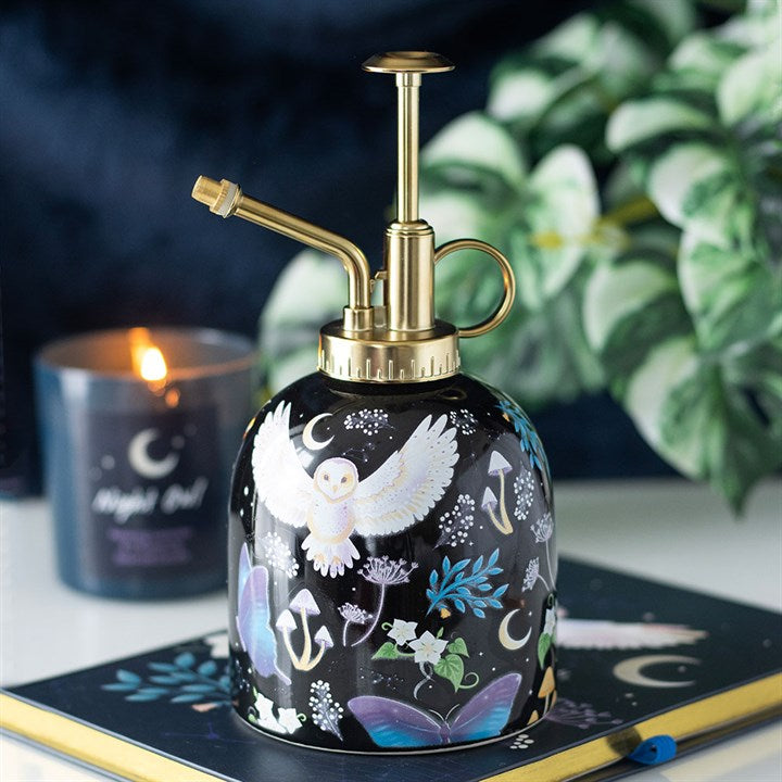 Decorative plant spray bottle with artistic design on a table with a candle and book in the background.