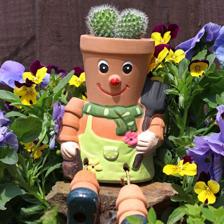 Terracotta pot character with a face, apron, and garden tools surrounded by flowers