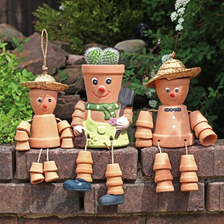 Three terracotta pot people with garden-themed accessories on a stone ledge.
