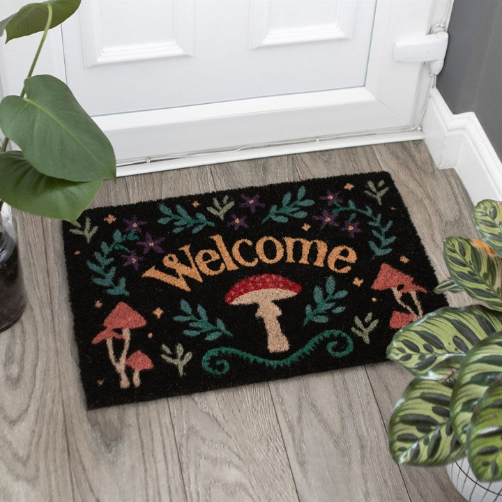 Decorative doormat with 'Welcome' and mushroom design on a wooden floor.