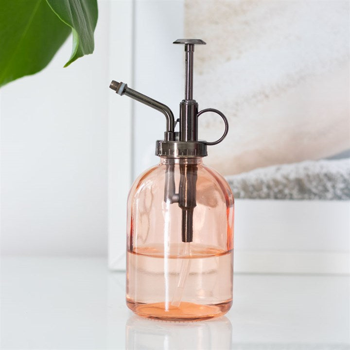 Pink glass spray bottle with black pump on a light surface.