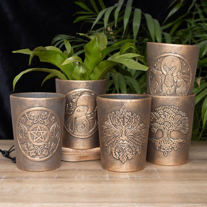Set of five bronze-colored  plant pots with embossed designs on a wooden surface with plants in the background.