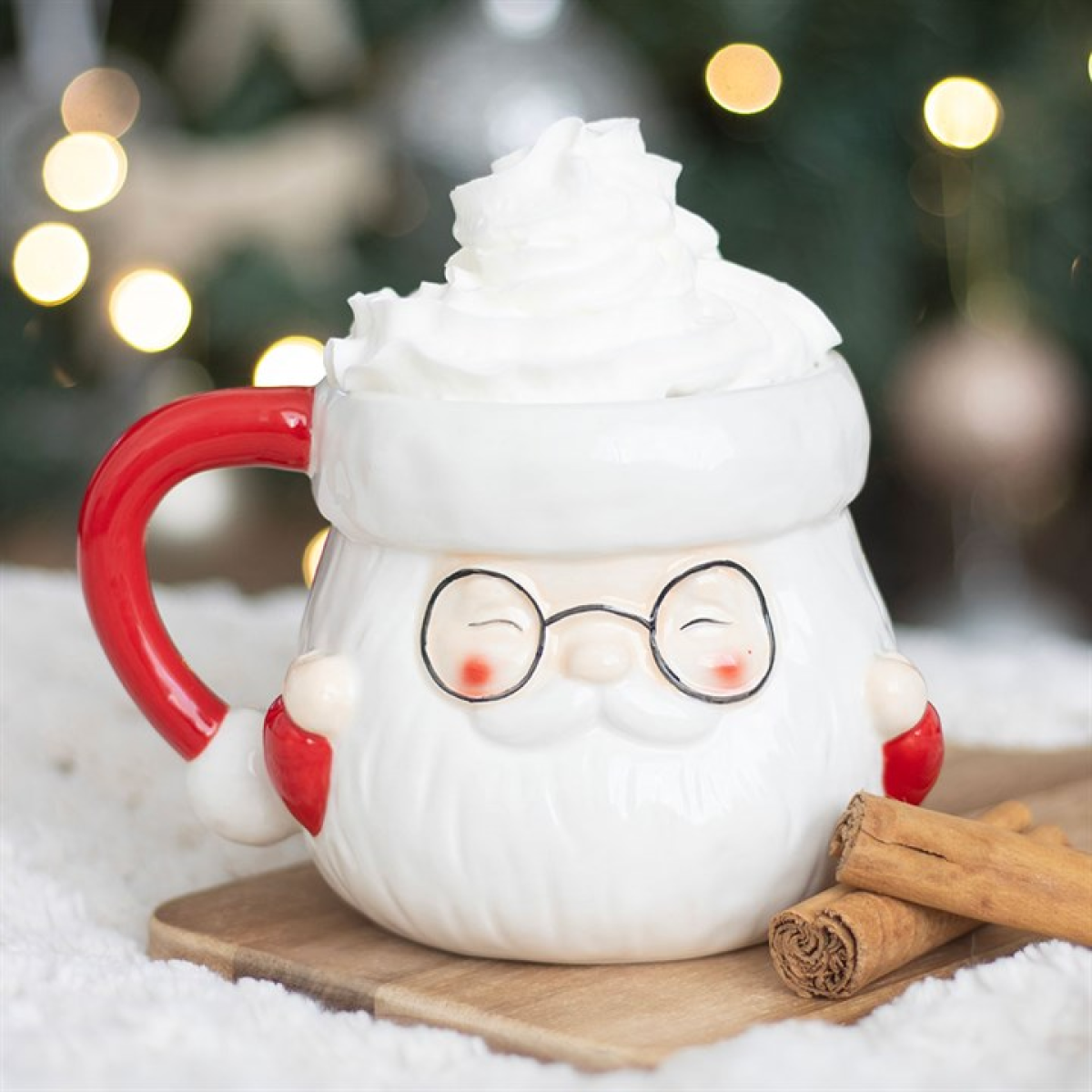 White mug with a cartoon face, red handle, and glasses, set against a festive background with lights and cinnamon sticks.