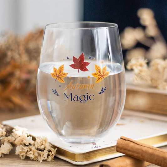 Clear glass with autumn-themed design featuring leaves and 'Autumn Magic' text, placed on a surface with decorative elements.