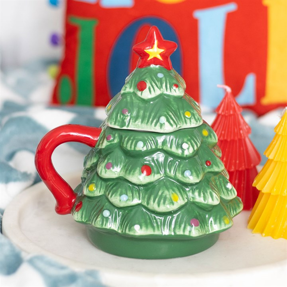 Christmas tree-shaped mug with a red handle and star on top, set against a colorful background.