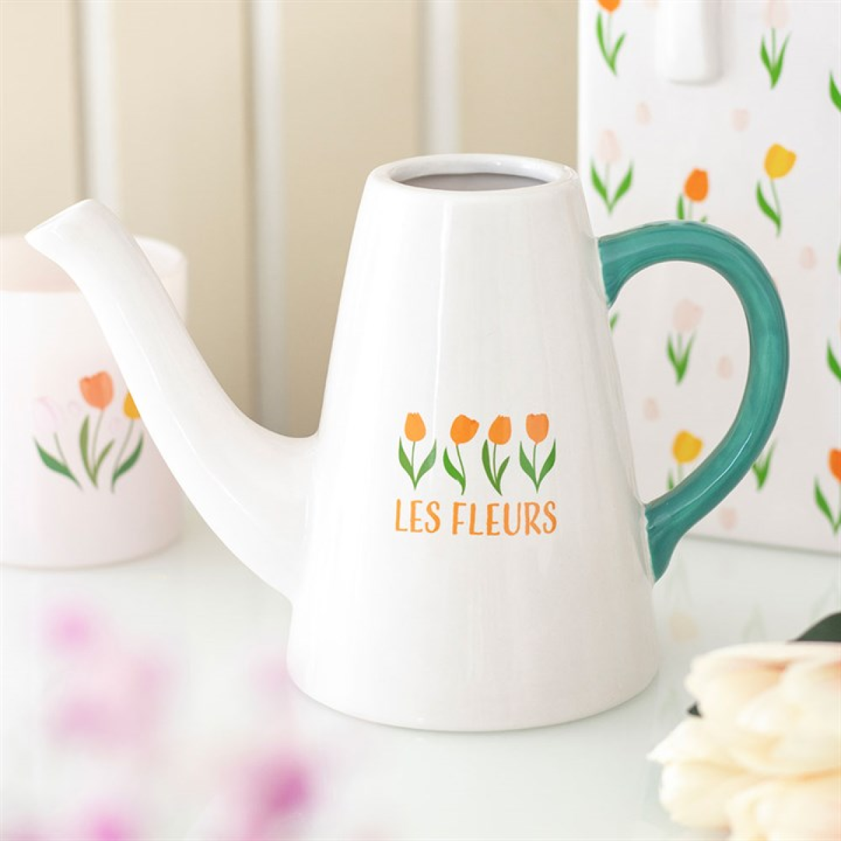 White watering can with green handle and 'Les Fleurs' branding on a floral background
