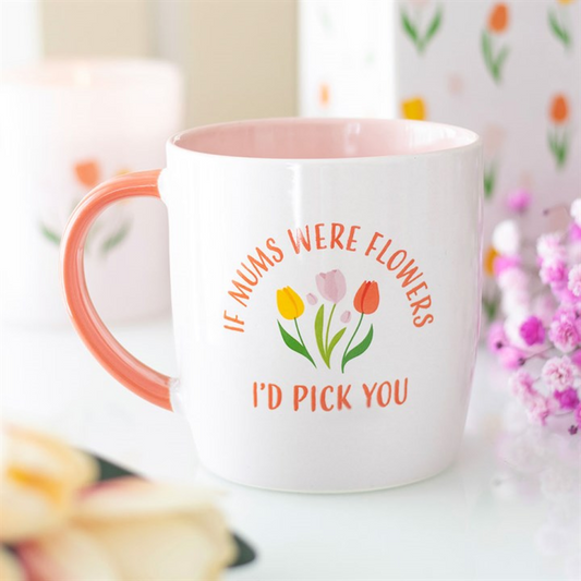 White mug with floral design and text, surrounded by flowers and blurred background