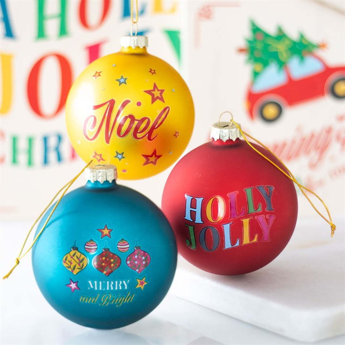 Three colorful Christmas ornaments with festive text on a blurred background