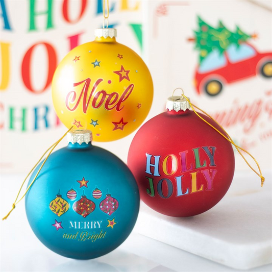 Three colorful Christmas ornaments with festive text on a blurred background