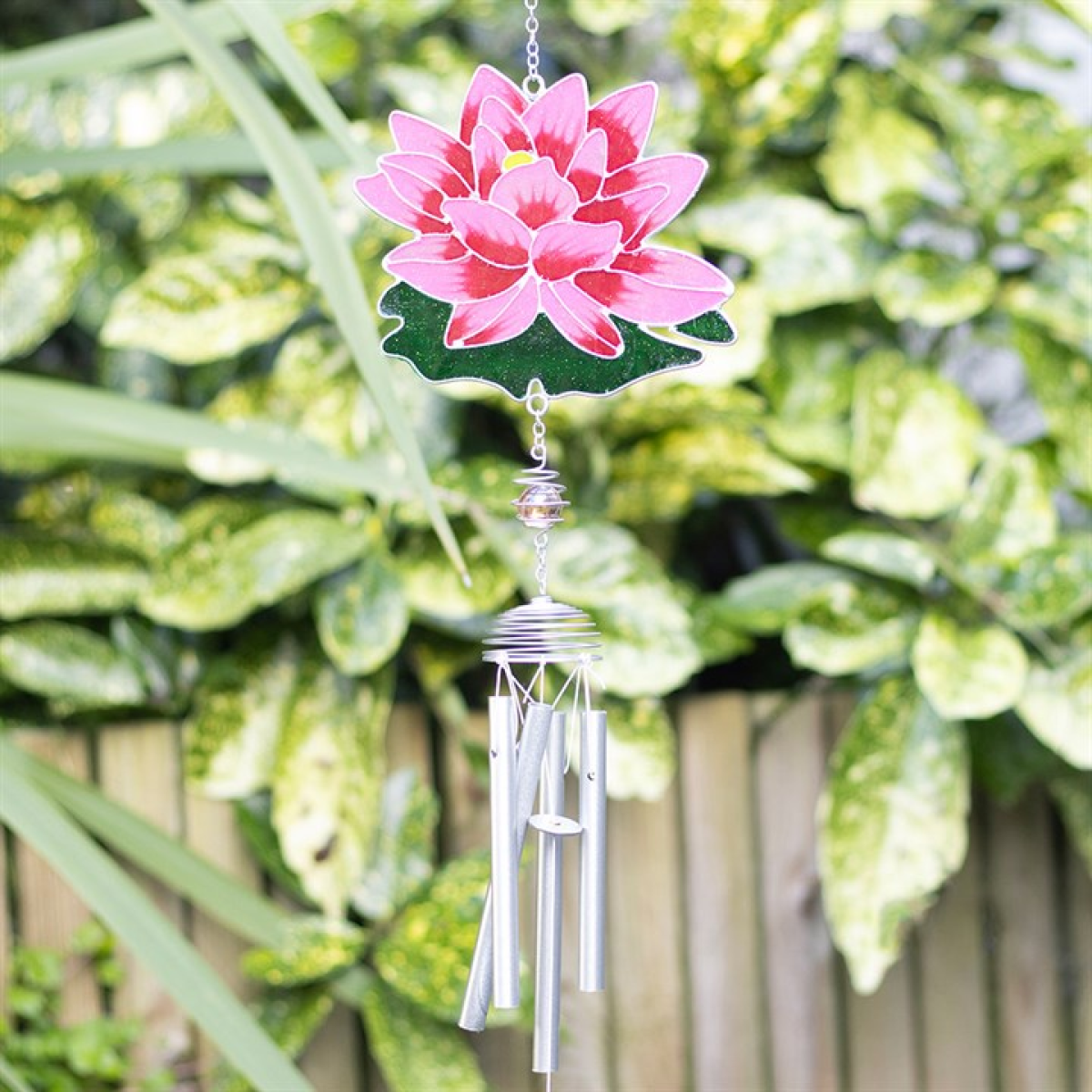 Decorative wind chime with pink flower design hanging among green foliage